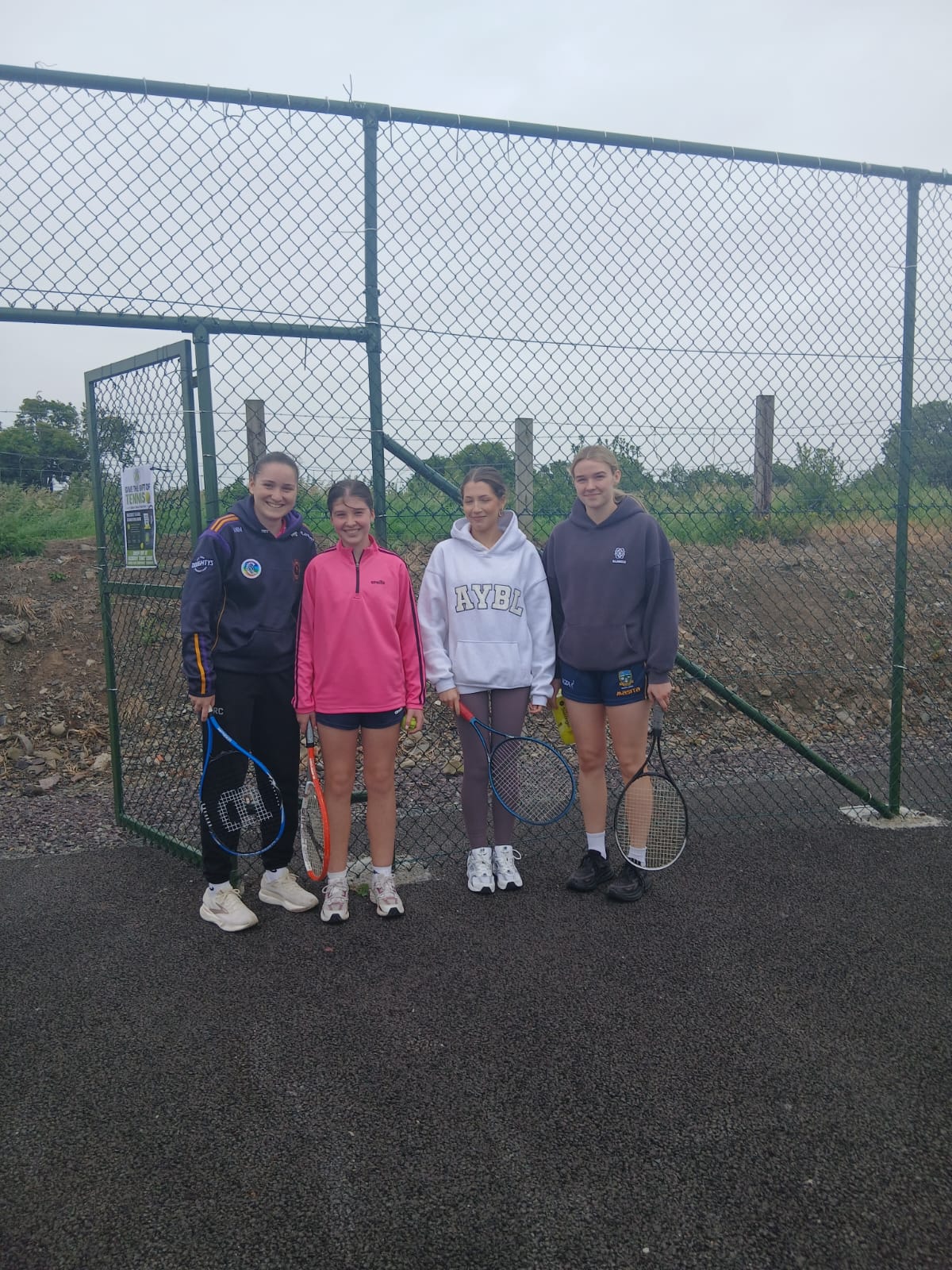 Four young members with racquets at the court gate